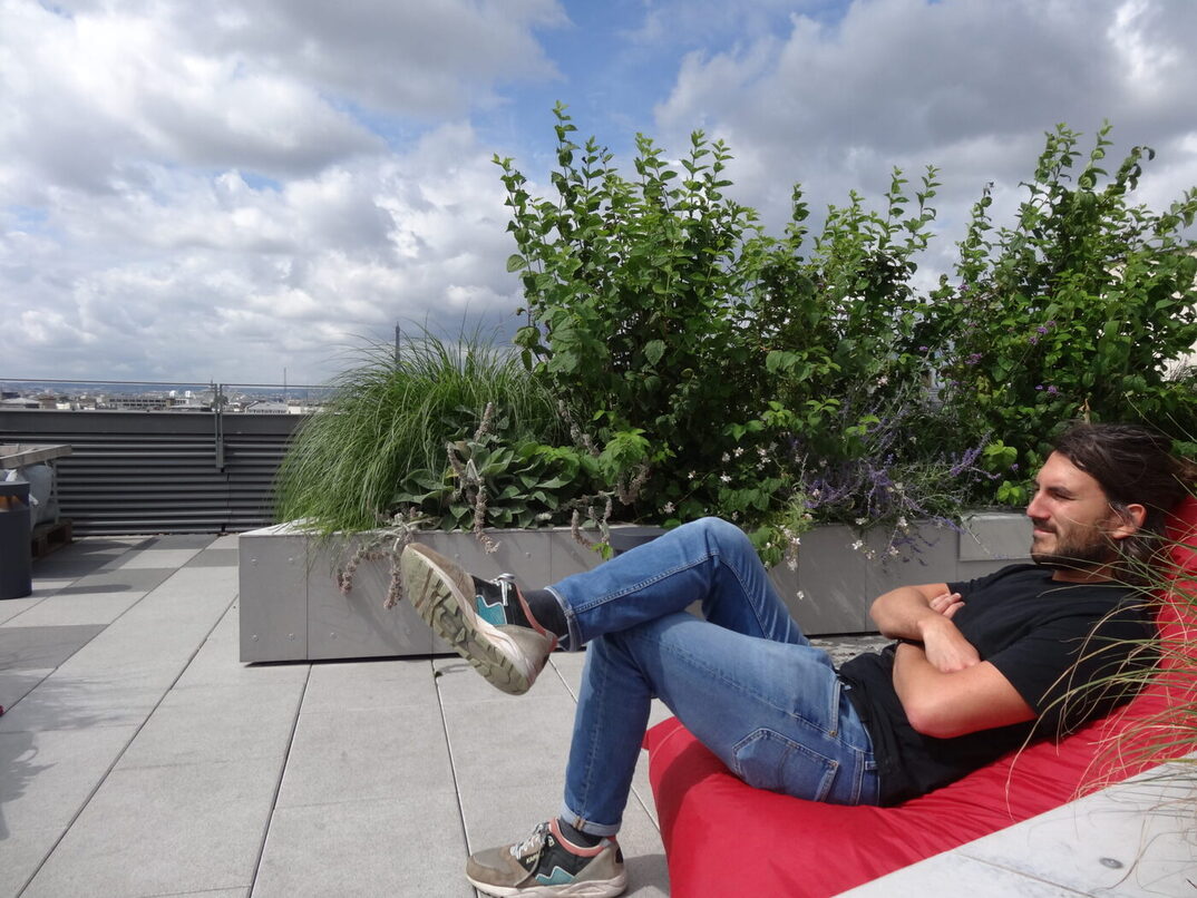 Un homme assis sur un beanbag rouge sur un rooftop au soleil