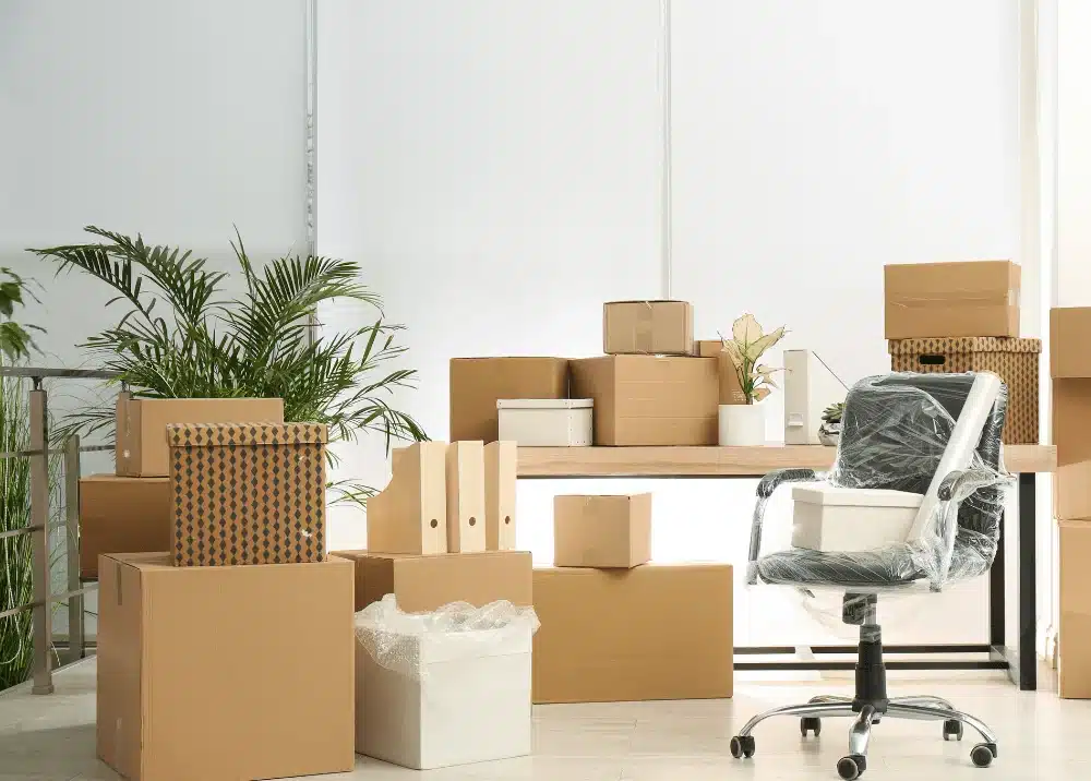 Cartons de déménagement et chaise de bureau emballée dans un bureau moderne avec plantes vertes