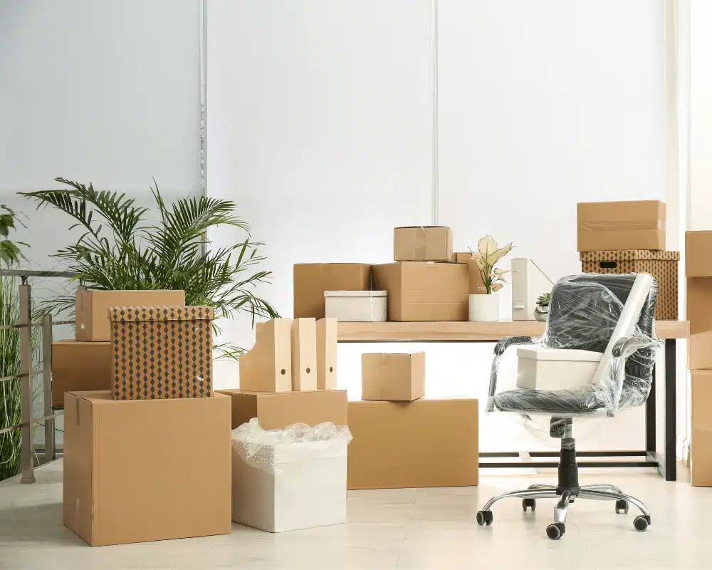Cartons de déménagement et chaise de bureau emballée dans un bureau moderne avec plantes vertes